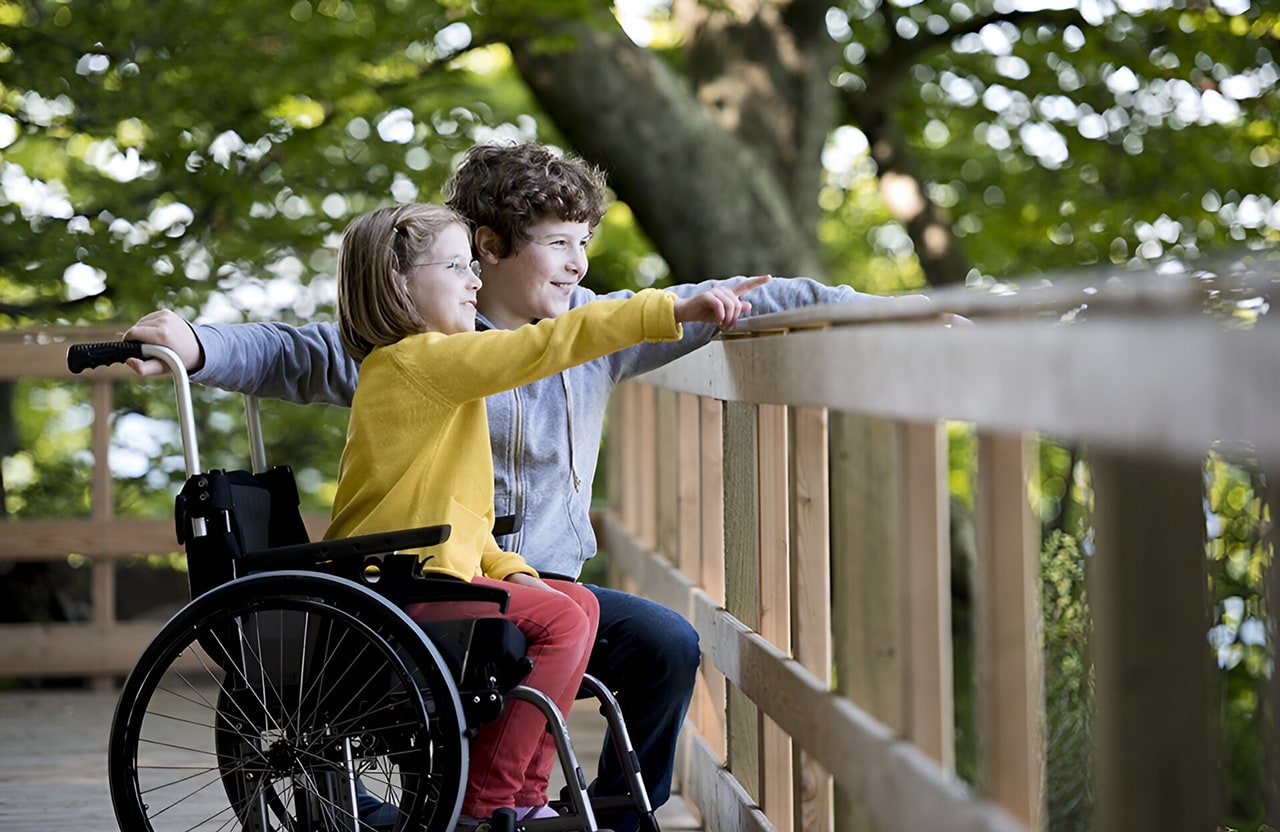 un garçon et une petite fille dans un fauteuil roulant qui regardent et pointent dans une direction